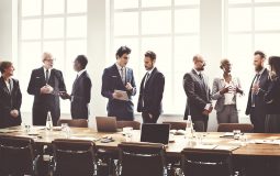 People in suits standing around a boardroom talking with each other