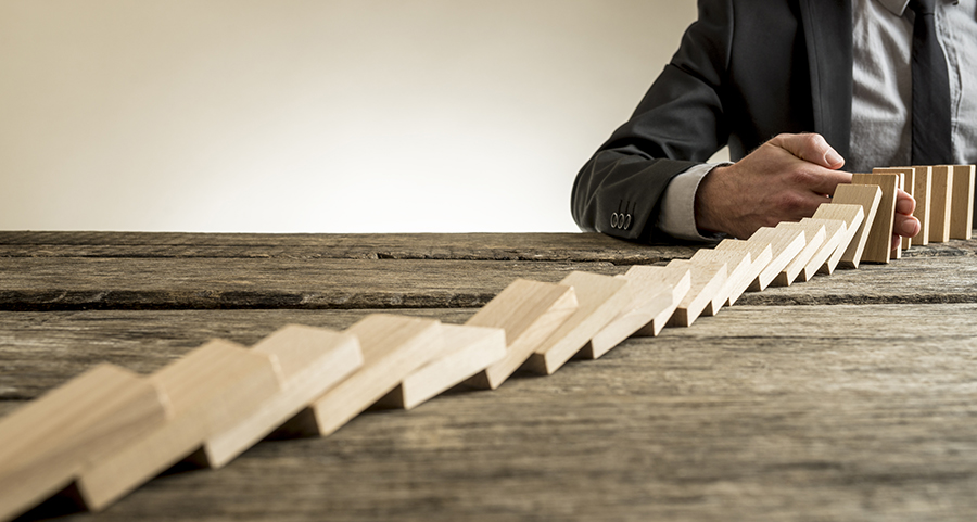 Image of blocks collapsing in a domino effect until being stopped, represents ability to use solutions and safeguards to prevent fraud destroying the business